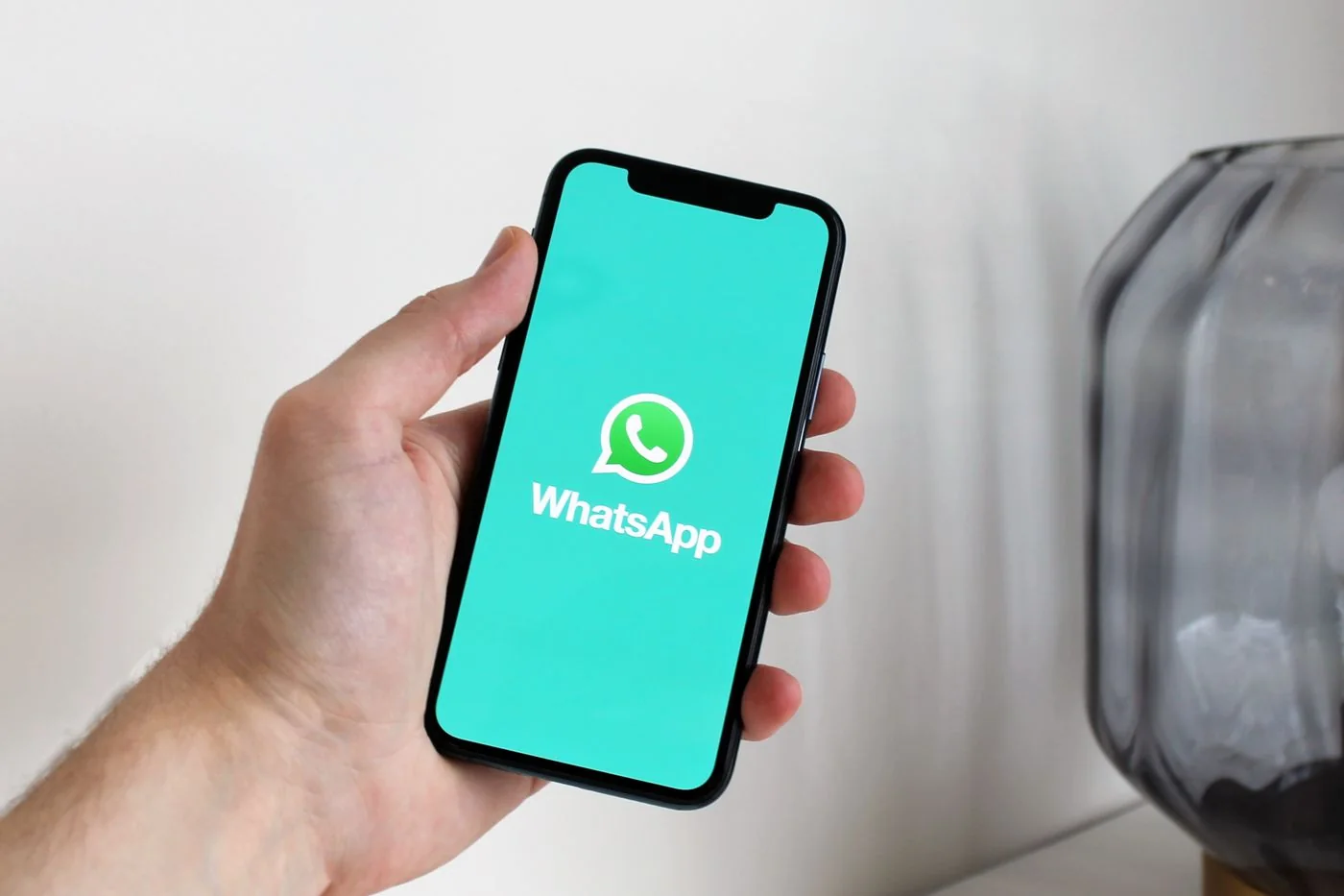 A hand holding a smartphone displaying the WhatsApp app