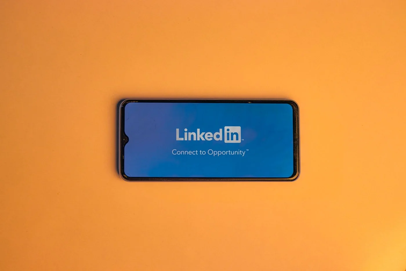 A smartphone displaying LinkedIn on an orange background