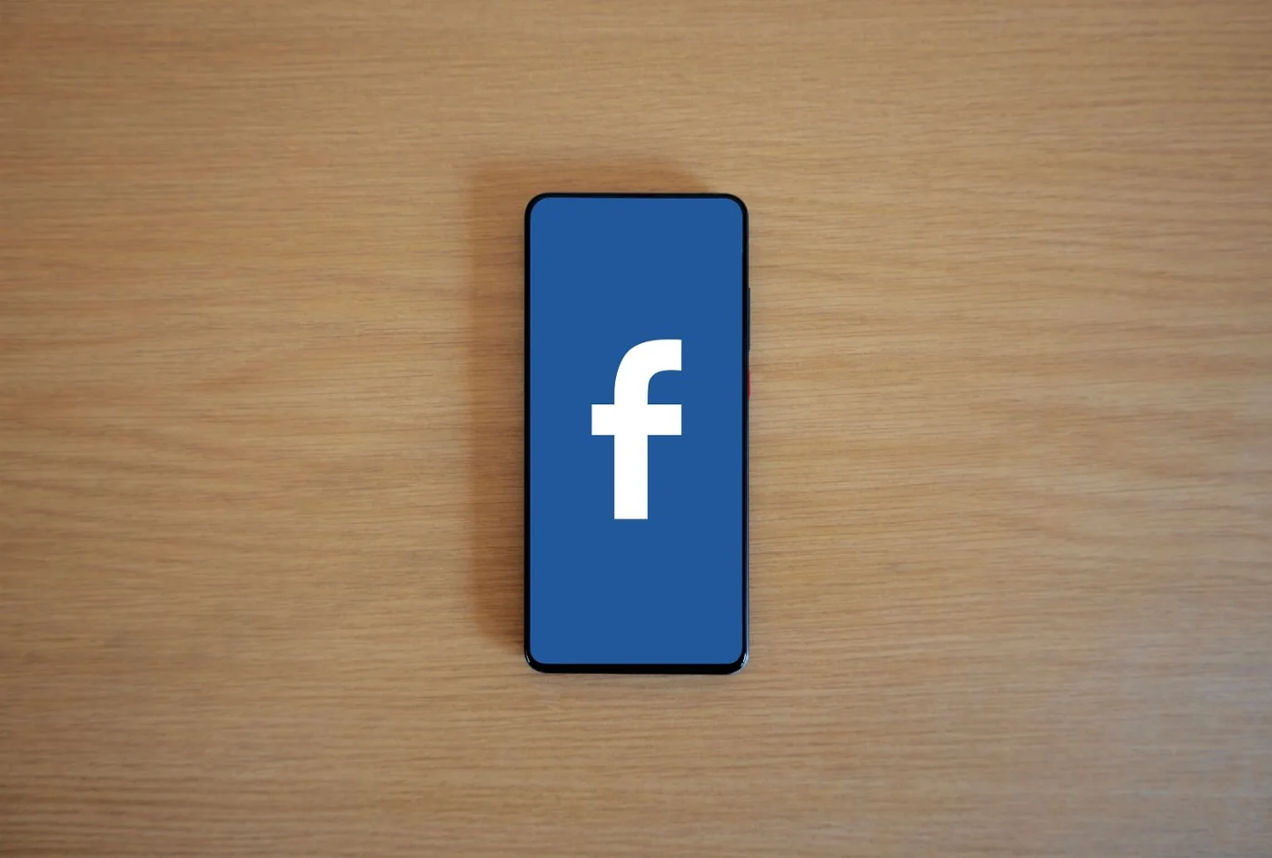 A smartphone displaying Facebook on a wooden desk