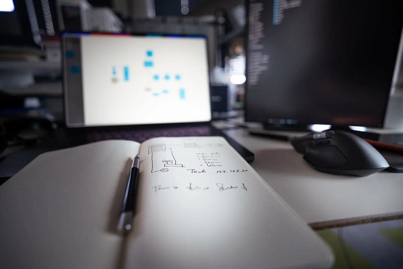 A notebook and pen beside monitors in a work area
