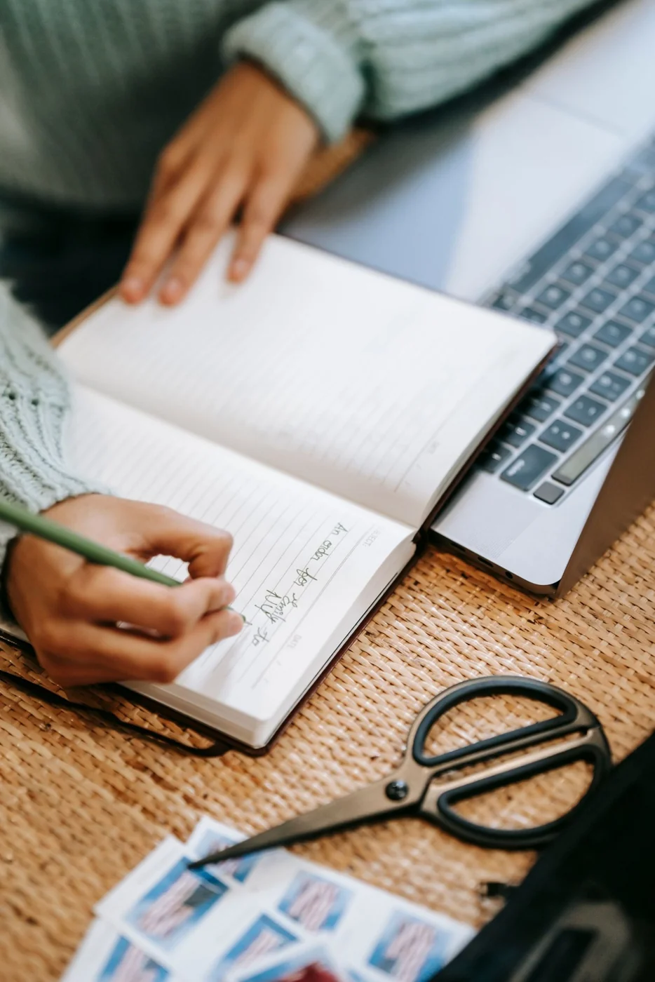 Hands writing content notes beside a laptop