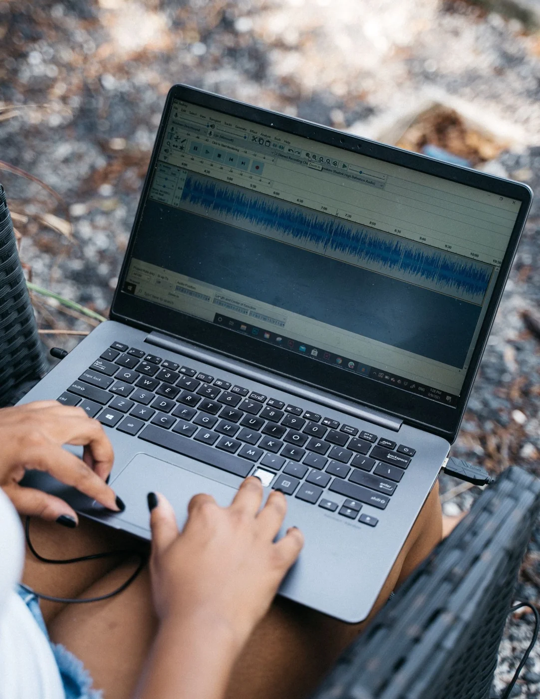 Hands editing audio on a laptop outdoors