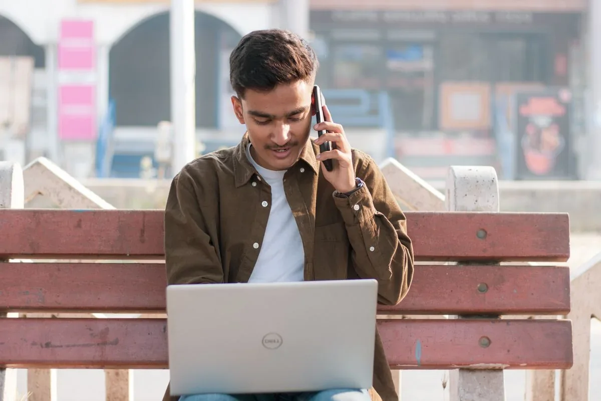 A professional working with a phone and laptop outdoors in India